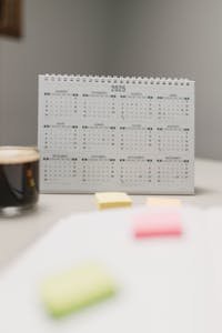 A 2025 spiral-bound desk calendar next to coffee and colorful sticky notes.