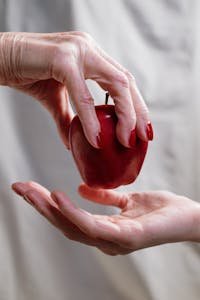 A close-up of two hands exchanging a red apple, symbolizing temptation or stories like Snow White.