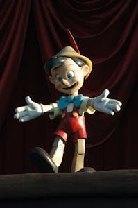 Charming wooden Pinocchio doll posed against a dramatic red curtain backdrop.